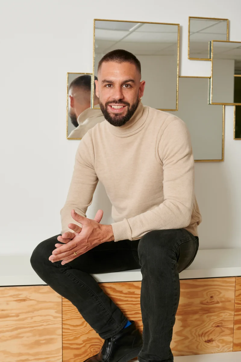 Antoine Andrieu assis, souriant, en col roulé beige.